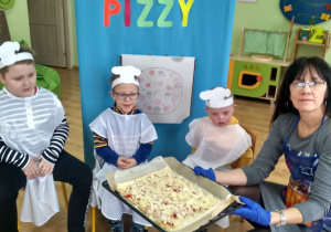 Dzieci razem ze swoją panią prezentują wykonaną pizzę.